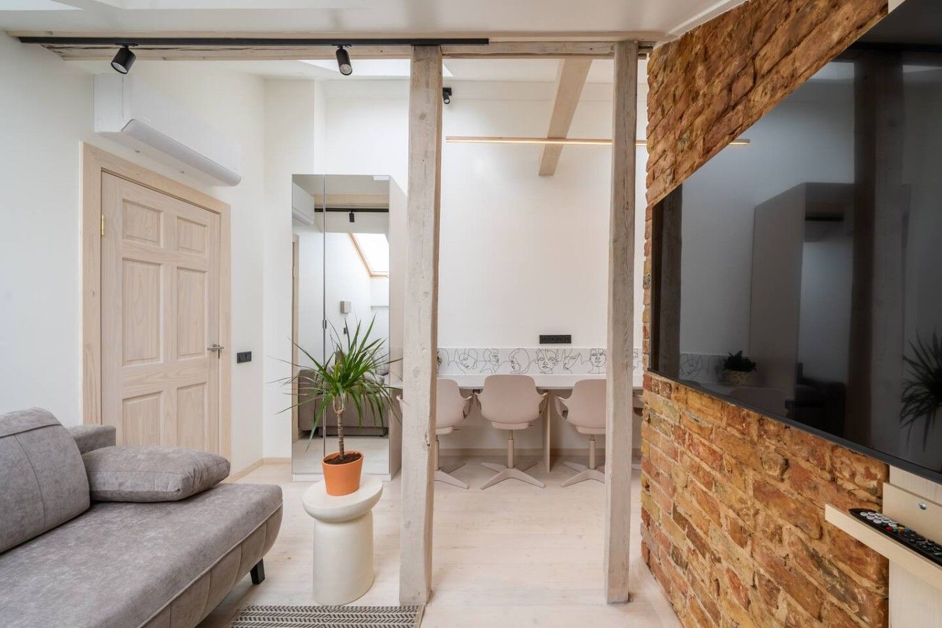 Een moderne woonkamer met een grijze bank, een potplant en een televisie bevestigd aan een bakstenen muur.