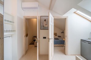 A compact bedroom with a bed, bedside table, and a hanging light fixture. - Stylish 2-Bedroom Attic Loft with AC & Workspaces (Rīga)