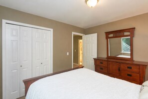 A bedroom with a bed, a dresser, a mirror, and a door leading to a hallway.