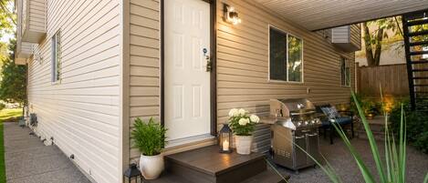 A single-story house with a front porch, a grill, and outdoor seating.