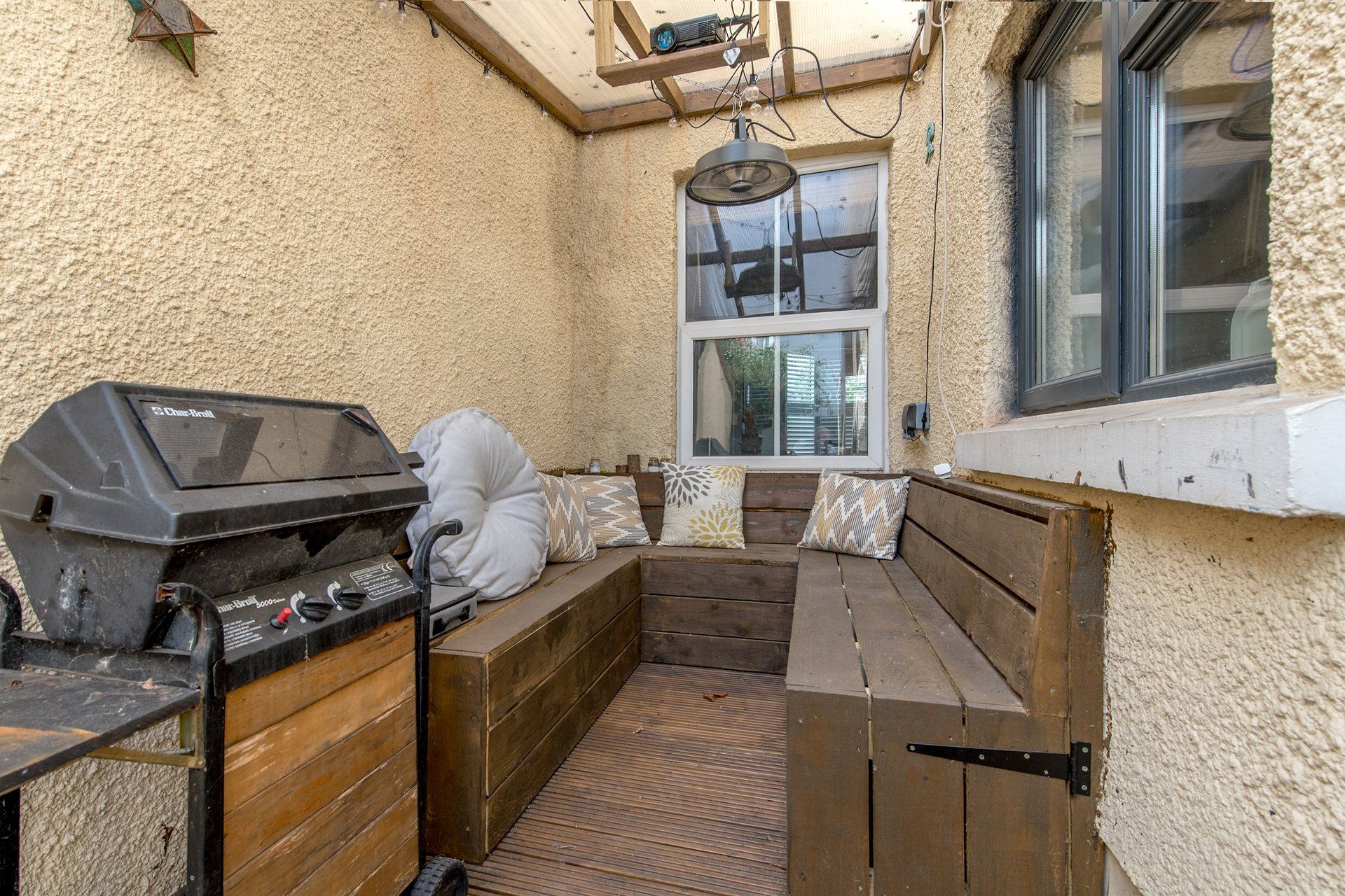 Une terrasse avec un barbecue, un banc en bois et une fenêtre.