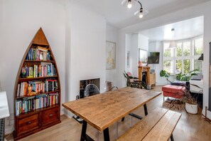 Um quarto espaçoso com uma mesa de madeira, estante, lareira e televisão.