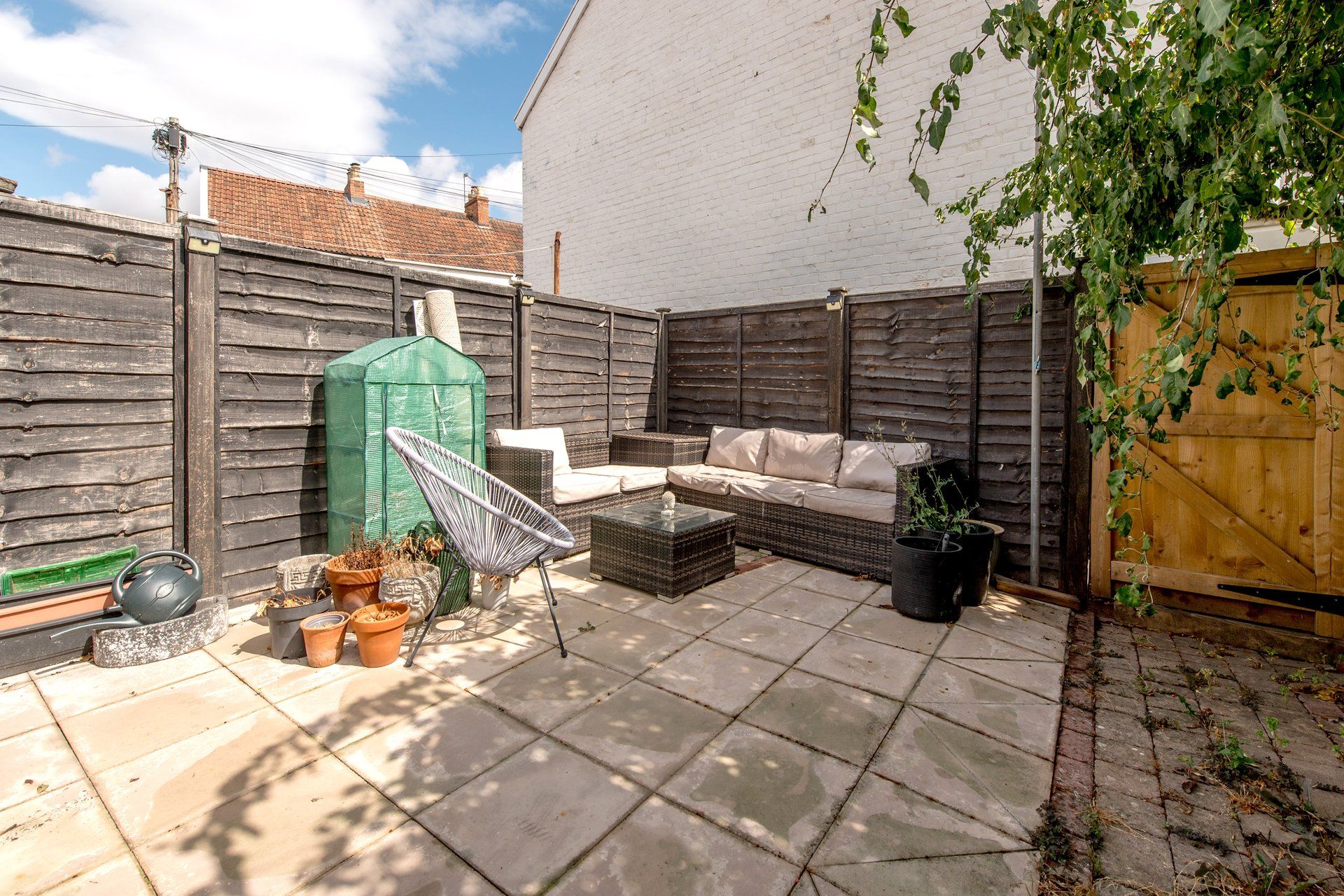 A patio area with a wicker sofa, a green garden box, and potted plants.