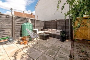 A patio area with a wicker sofa, a green garden box, and potted plants. - 2BR House with Courtyard Garden Near Taunton Rail (Taunton)