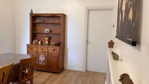 Una habitación con un armario de madera, una mesa de comedor con sillas, una puerta blanca y un cuadro colgado en la pared.
