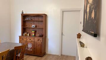 A room with a wooden cabinet, a dining table with chairs, a white door, and a wall-mounted picture.