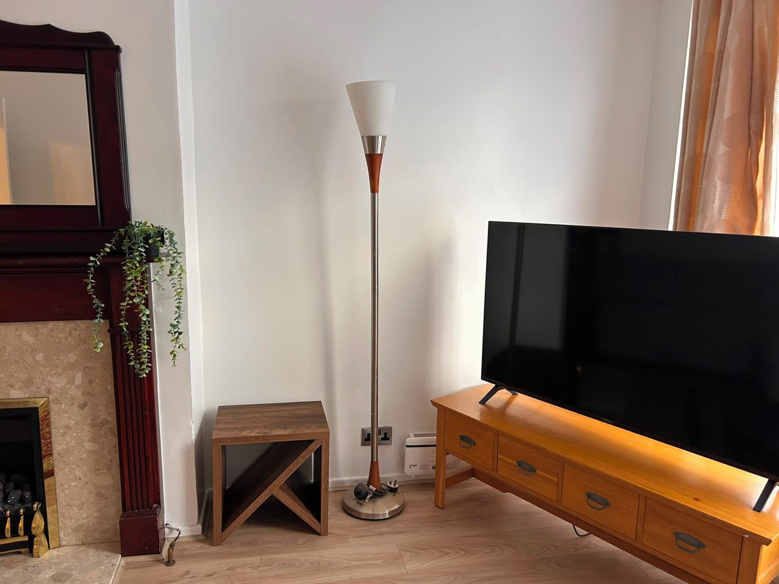 A living room with a television, a floor lamp, a small wooden table, and a fireplace.