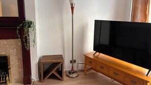 Una sala de estar con televisor, lámpara de pie, una mesita de madera y chimenea.