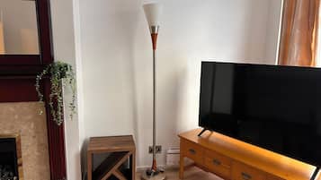A living room with a television, a floor lamp, a small wooden table, and a fireplace.