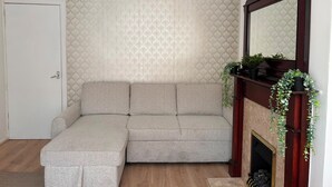 Una habitación de esquina con sofá modular, chimenea con espejo y papel tapiz estampado.