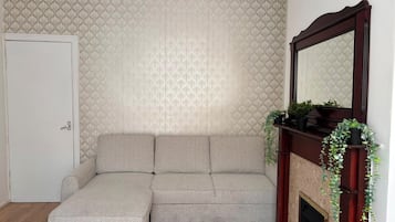 A corner room with a sectional sofa, a fireplace with a mirror, and a patterned wallpaper.