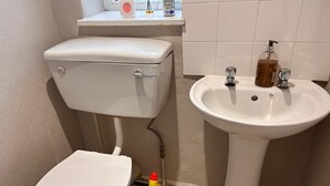 Un baño con inodoro, lavamanos y una botella de producto de limpieza en el suelo.