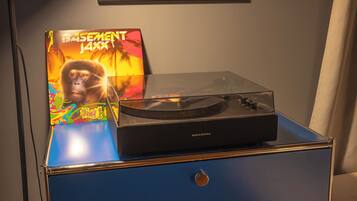 A turntable on a blue cabinet with a record sleeve labeled 'Basement Jazz' and a painting above it.