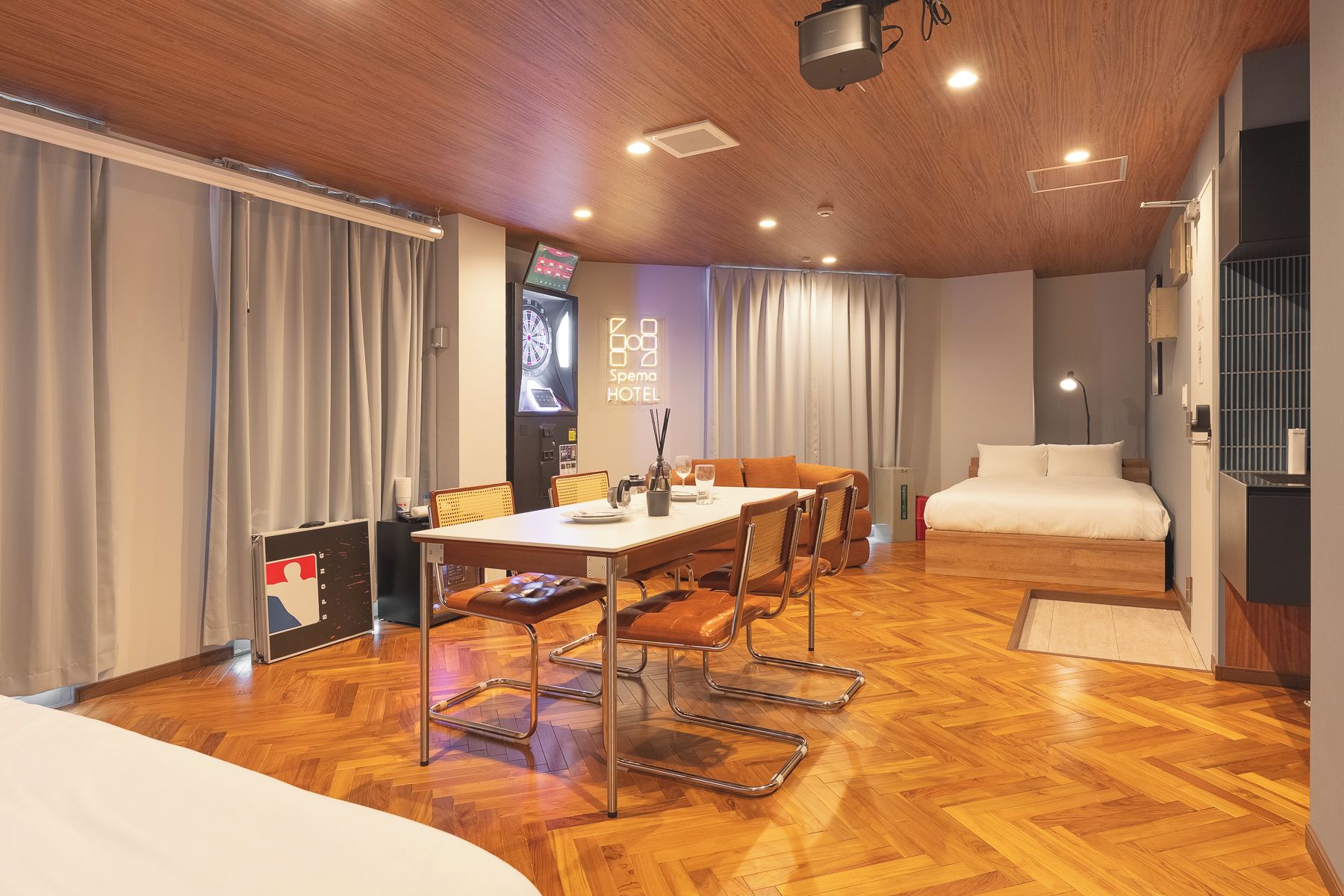 Habitación de hotel con piso de madera, una cama, una mesa de comedor con sillas, un televisor y un cartel en la pared.