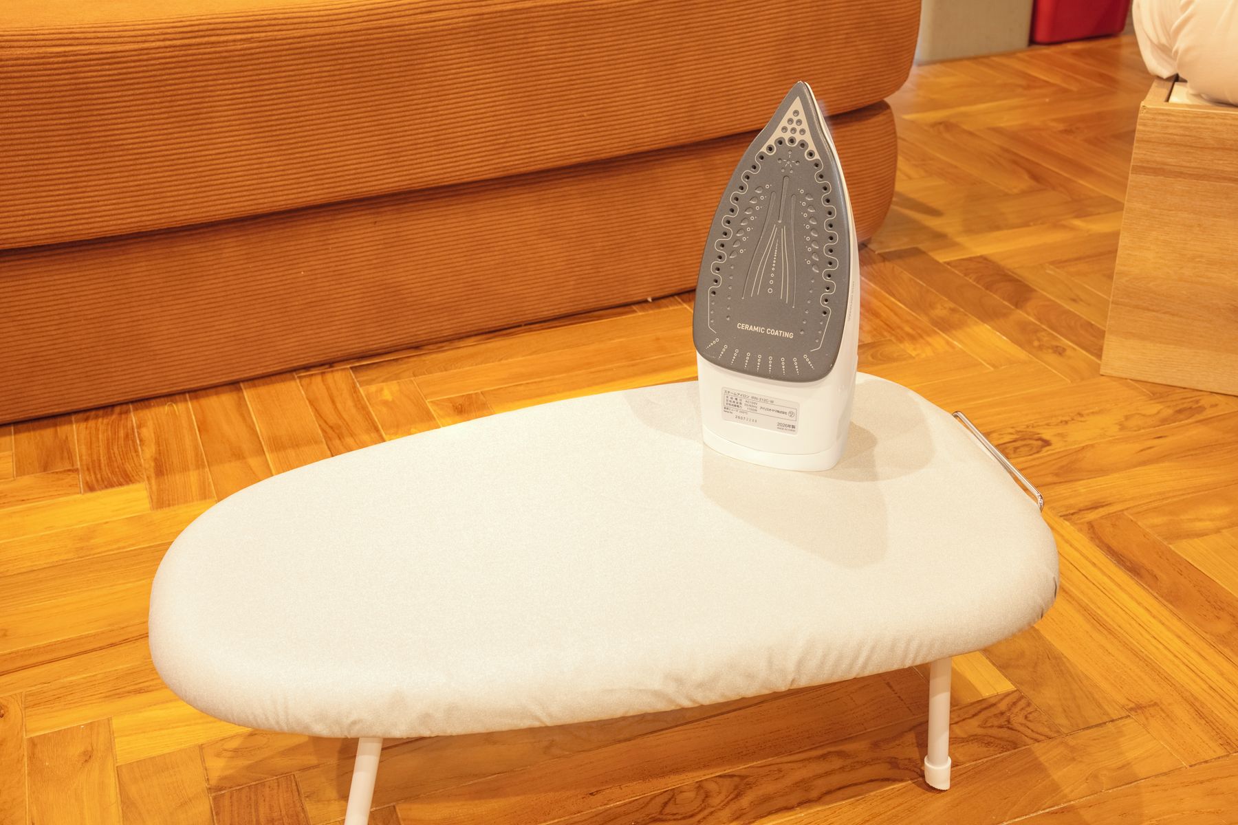 A white ironing board with a ceramic coating on the base, placed on a wooden floor.