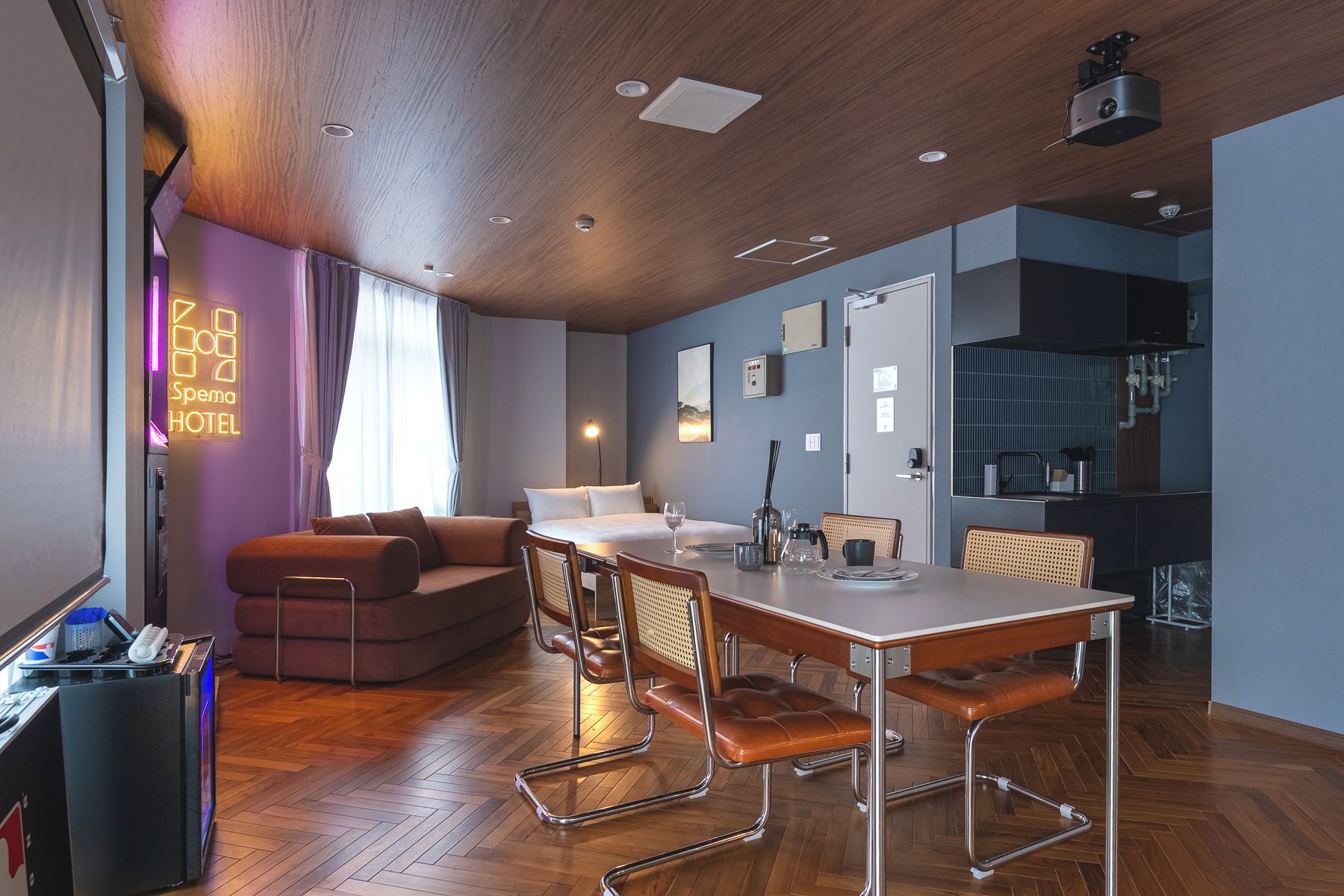 A hotel room with a wooden ceiling, a dining area with a table and chairs, a sofa, and a bed.