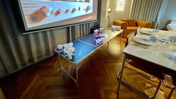 A room with a pool table, a projector screen displaying a presentation, a dining table set for two, and a sofa.
