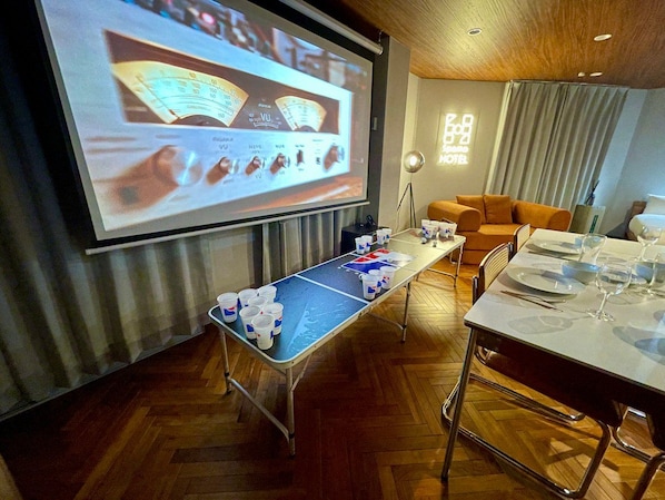 A room with a pool table, a projector screen displaying a presentation, a dining table set for two, and a sofa. - SpemaHOTEL Kinshicho 4F (Sumida City)