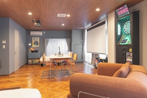 Una habitación con techo de madera, una mesa de comedor con sillas, un sofá, un dardo y una pantalla de proyector.