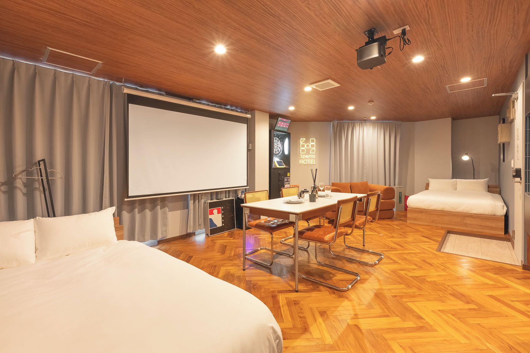 Ett hotellrum med en stor säng, en mindre säng, ett skrivbord med en stol, en tv och en takprojektor.