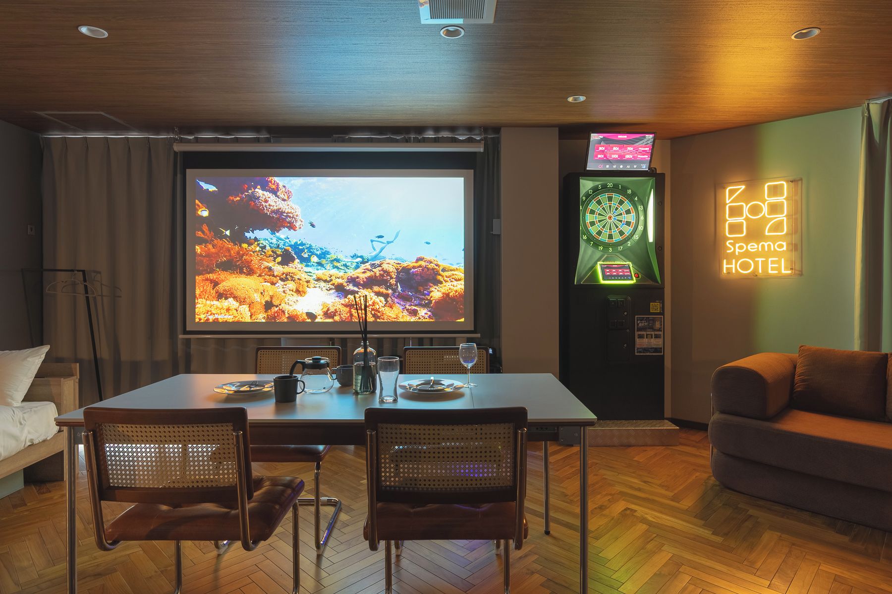 A hotel room with a large screen displaying a scenic view, a dartboard, and a Spema Hotel sign.