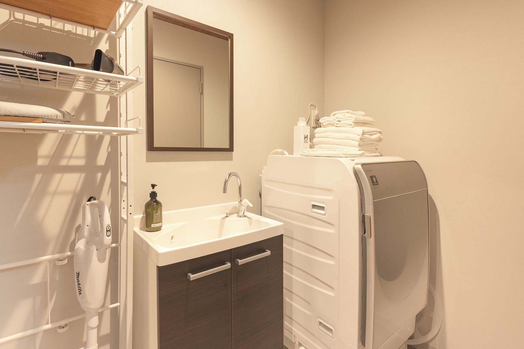 Un baño con lavamanos blanco, un espejo, dispensador de toallas y un montón de toallas.