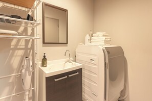 A bathroom with a white sink, a mirror, a towel dispenser, and a towel stack.