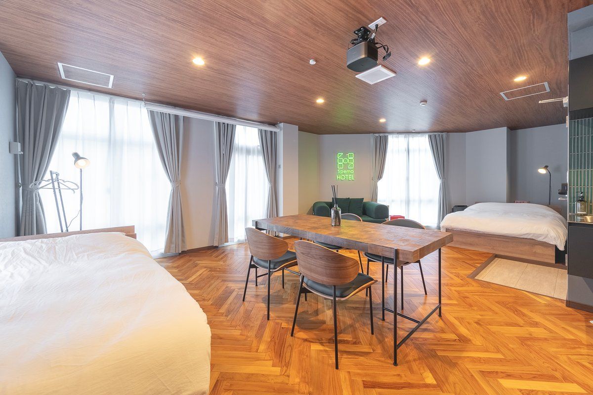 A hotel room with a wooden ceiling, a dining table with chairs, a bed, and a large window with curtains.