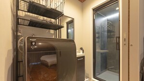 A compact room with a built-in washer-dryer unit, a small bed, and a sliding glass door leading to a shower area.