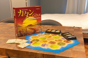 A board game setup on a wooden table with a game box labeled 'CATAN' and various game pieces.