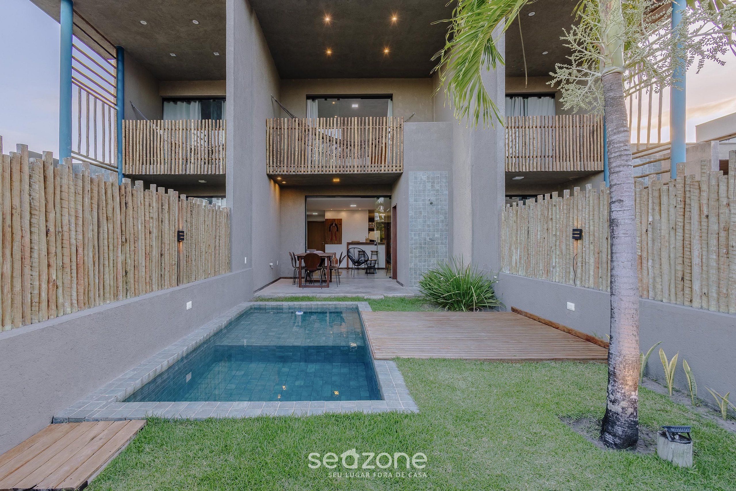 A modern outdoor pool area with a wooden deck, a small grassy area, and a bamboo fence.