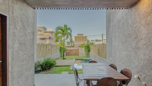 A covered patio with a wooden table and chairs, a small pool, and a view of a residential area with houses and palm trees. - House w 3 Suites n Pool 100m From the sea Hva0009 (Passo de Camaragibe)