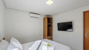 Una habitación de hotel con cama, armario, televisor de pantalla plana montado en la pared y aire acondicionado.