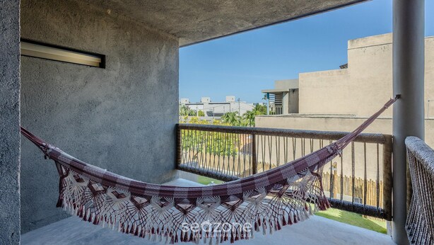 Una hamaca en un balcón con techo de hormigón y barandillas metálicas, con vistas a una zona residencial.