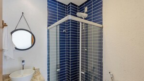 Un baño con un lavamanos blanco, un espejo y una ducha con paredes de azulejos azules.