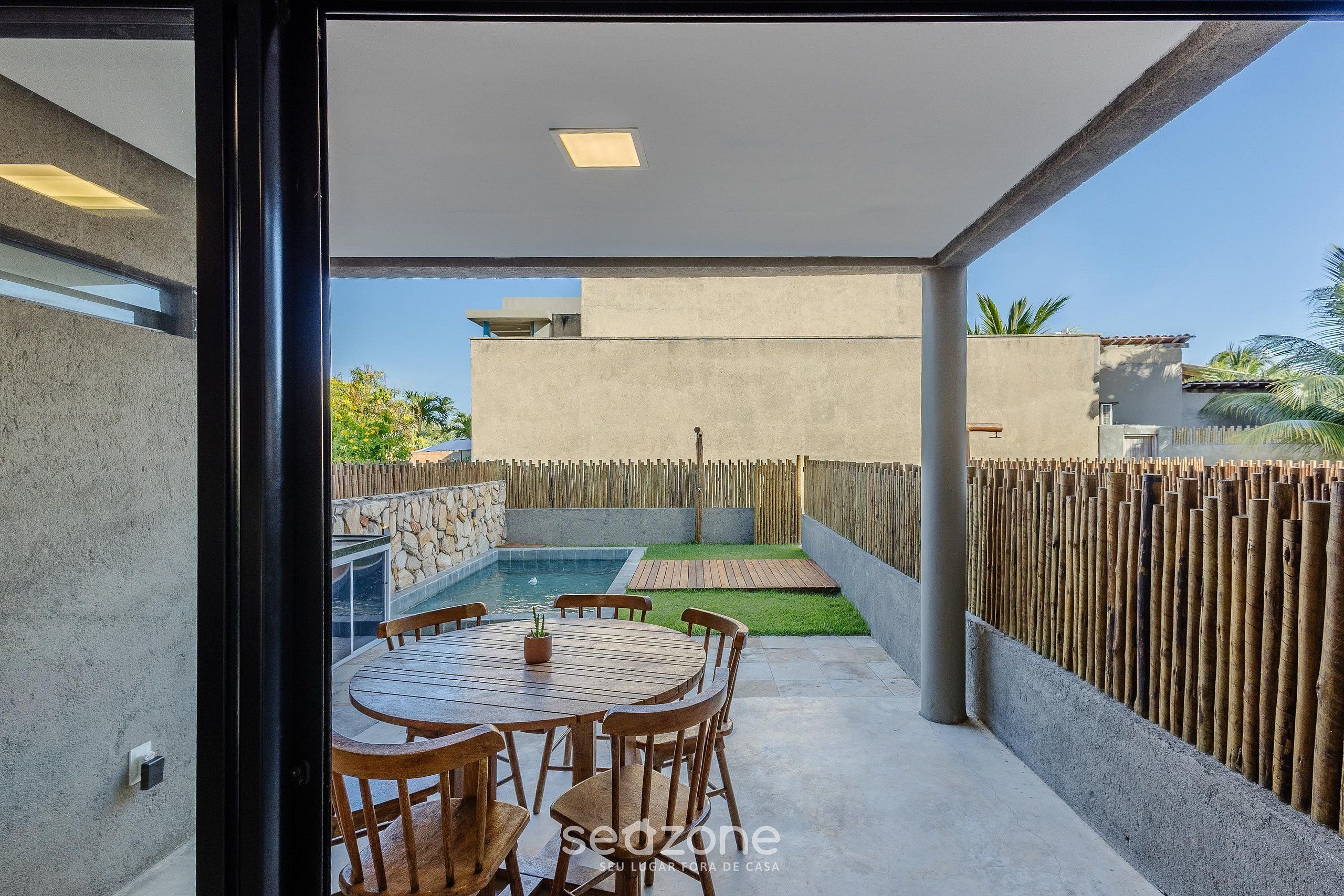 A modern outdoor patio with a round wooden table and chairs, a small pool, and a wooden fence.