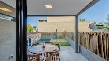 A modern outdoor patio with a round wooden table and chairs, a small pool, and a wooden fence.