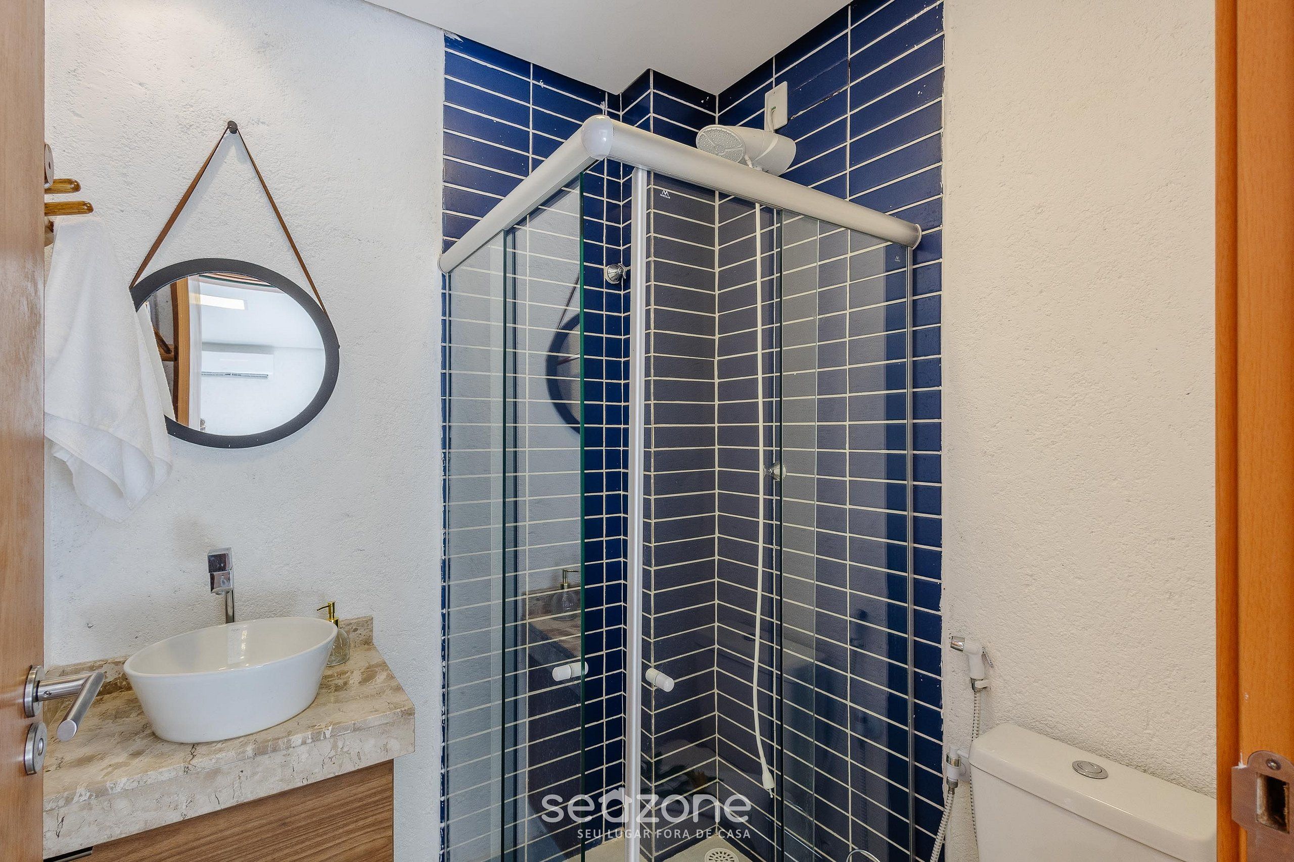 A bathroom with a white sink, a mirror, and a shower with blue tiles.