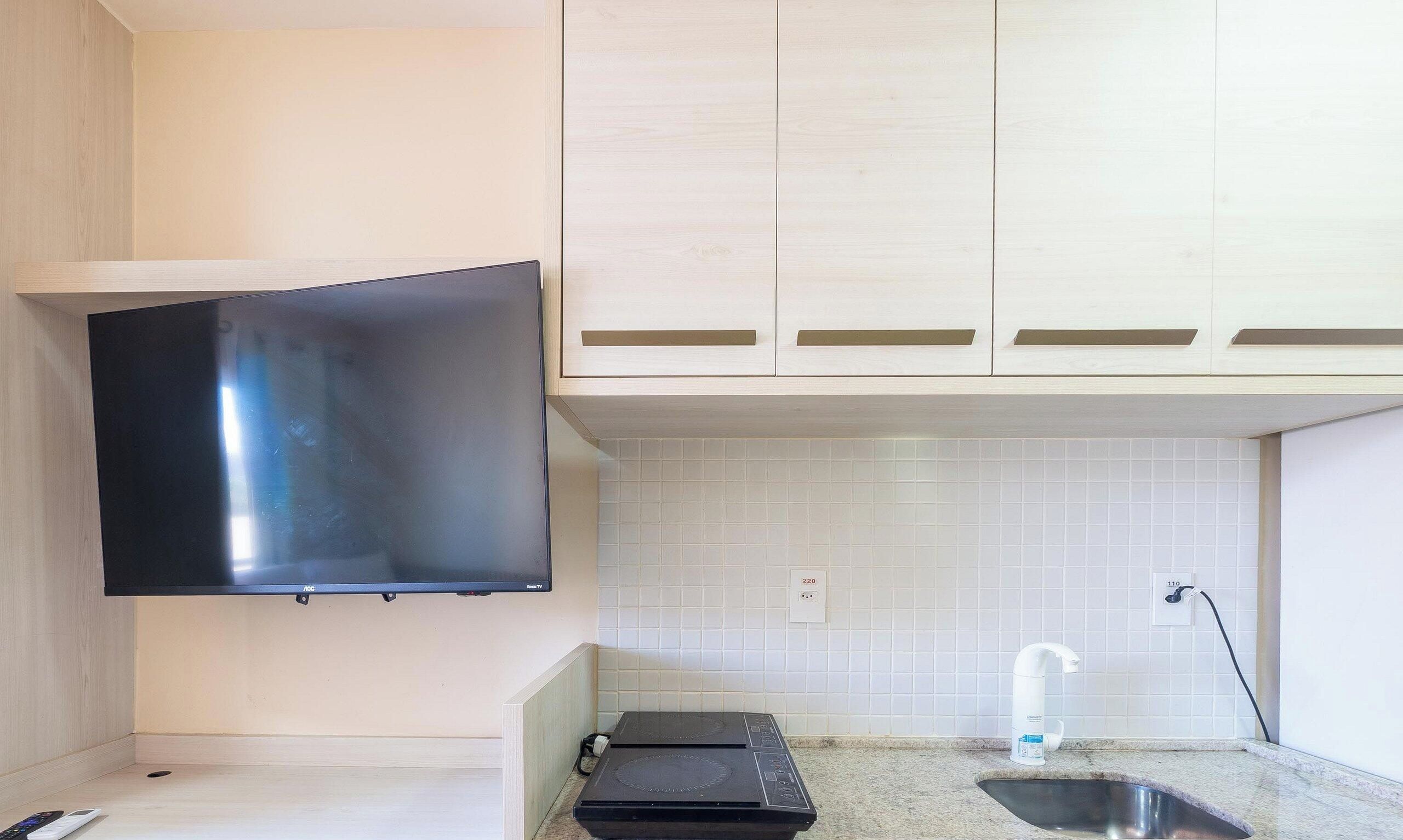 Una cocina con una televisión de pantalla plana montada en la pared, un lavamanos y una encimera.