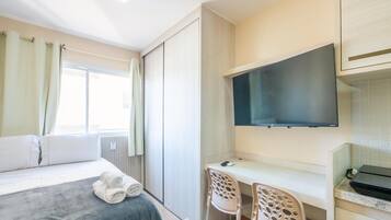 Une chambre d’hôtel comprenant un lit, un bureau avec deux chaises, un téléviseur à écran plat et une fenêtre avec des rideaux.