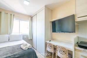 Une chambre d’hôtel comprenant un lit, un bureau avec deux chaises, un téléviseur à écran plat et une fenêtre avec des rideaux.