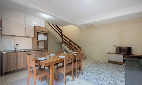 Espaço compacto com cozinha, área de refeições e escada que leva a um andar superior.