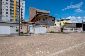 A residential street with a two-story house featuring a balcony, a white fence, and a paved road. - House in Condo w/ Pool Steps From the sea Oni0002 (Barra Velha)