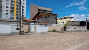 A residential street with a two-story house featuring a balcony, a gated entrance, and a paved road.