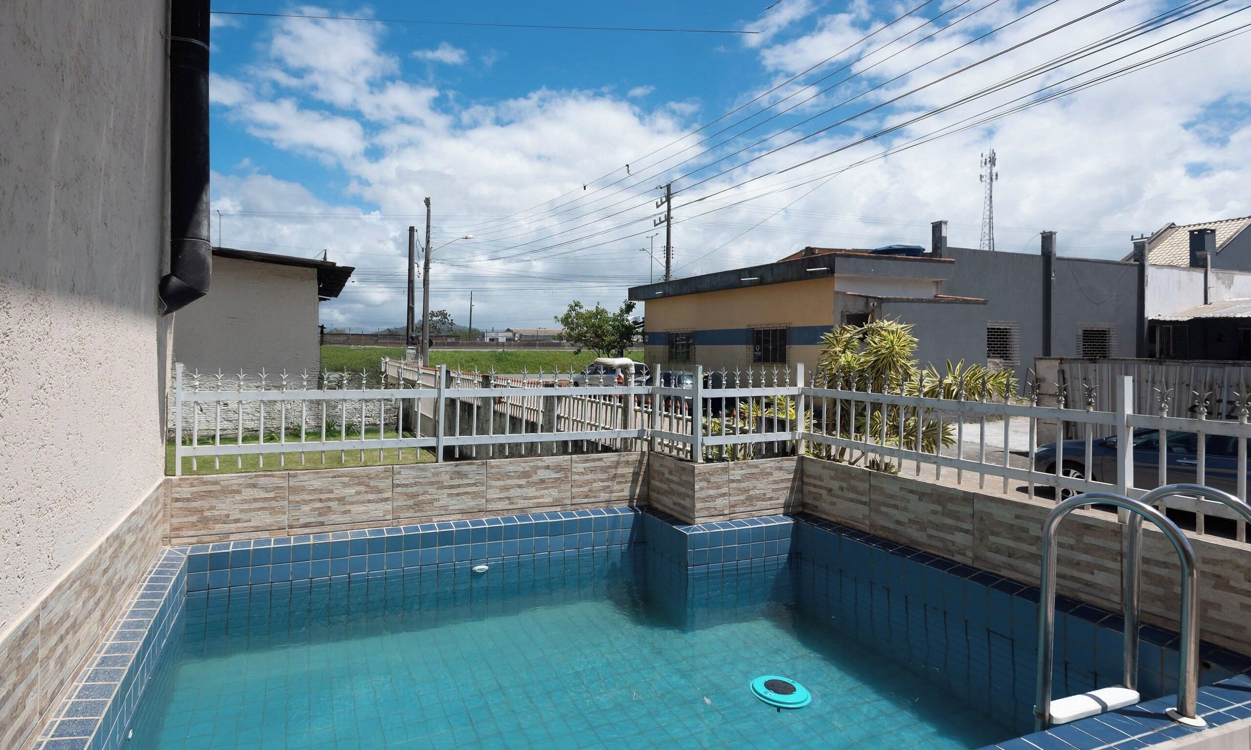 A swimming pool with a tiled edge, surrounded by a white fence, and a clear blue sky in the background.