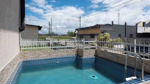 A residential swimming pool with a tiled deck, surrounded by a white fence, and utility poles in the background.