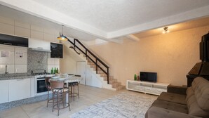 Et moderne køkken med spiseplads, en trappe og en stue med sofa og tv.