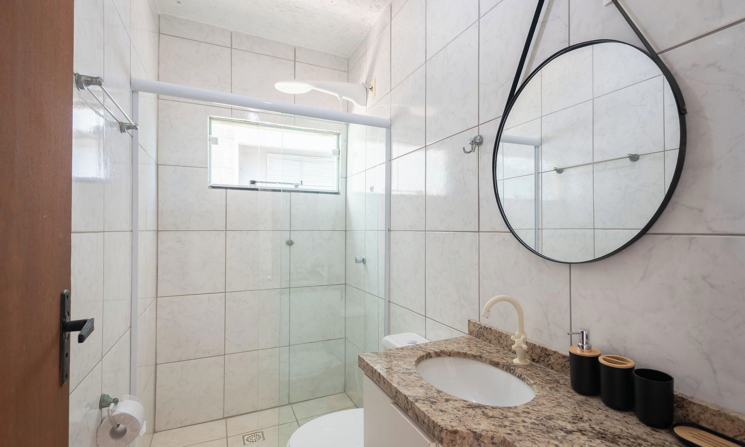 A bathroom with a glass-enclosed shower, a sink with a marble countertop, and a round mirror.