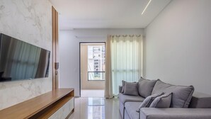 Ett modernt vardagsrum med en platt-TV som är monterad på en vägg av marmor, en grå soffa med kuddar och en skjutdörr i glas som leder ut till en balkong.