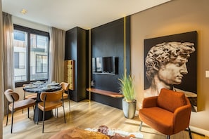 A modern living room with a round dining table, orange chairs, a large painting, a flat-screen TV, and a potted plant. - Modern Apartment Facing Praca das Etnias Cbg0306 (Gramado)